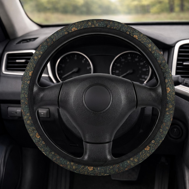 May include: A black steering wheel with a floral patterned cover. The cover features a dark green background with small yellow and blue flower designs. The steering wheel is in a car interior.