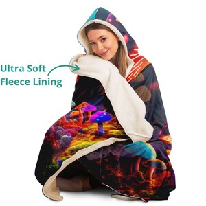 May include: A hooded blanket with a colorful mushroom design. The blanket features an ultra-soft fleece lining and a vibrant illustration of glowing mushrooms in shades of purple, blue, and orange against a dark background.