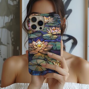 May include: A phone case with a stained glass design featuring water lilies and lily pads in shades of blue, green, yellow, and purple.