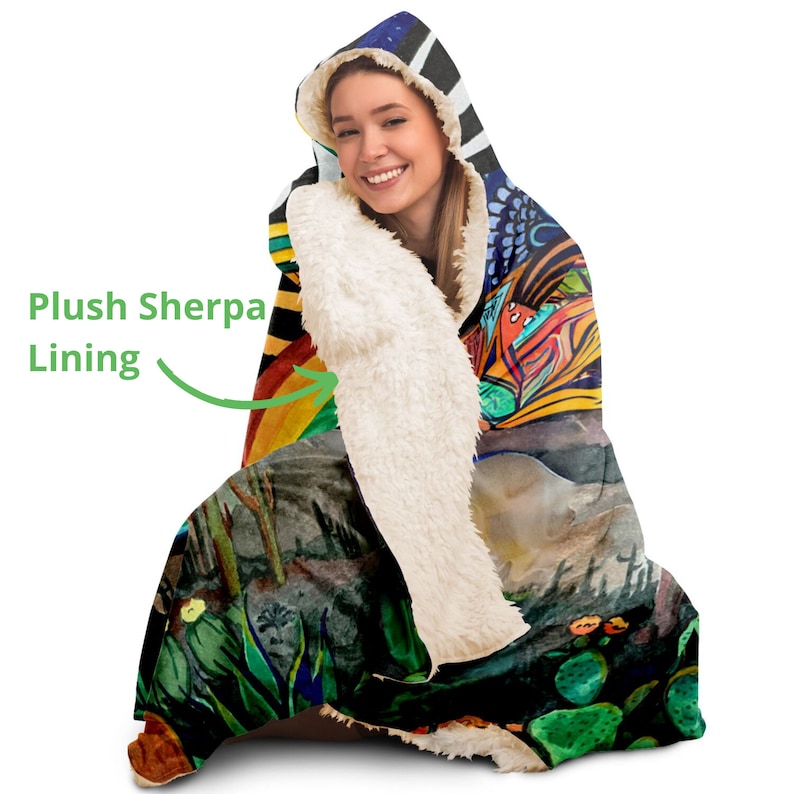 May include: A hooded blanket with a colorful, artistic design. The blanket features a plush sherpa lining for added warmth and comfort. The design includes a variety of colors and patterns, creating a unique and eye-catching look.