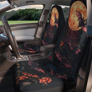 May include: Car seat covers featuring a spooky design with bats, a full moon, and roses. The seat covers are black with a dark red and orange color scheme. The interior of the car is visible, with a steering wheel and dashboard.