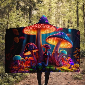 May include: A hooded blanket featuring a vibrant illustration of glowing, colorful mushrooms. The design includes red, orange, blue, and purple mushrooms with dotted caps, set against a dark, forest-like background. The blanket is hooded.