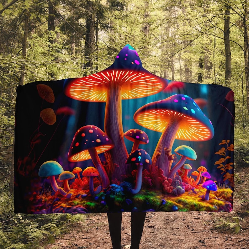 May include: A hooded blanket featuring a vibrant illustration of glowing, colorful mushrooms. The design includes red, orange, blue, and purple mushrooms with dotted caps, set against a dark, forest-like background. The blanket is hooded.