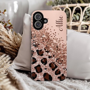 May include: A pink and gold glitter phone case with a leopard print design. The case has a cutout for the camera and the name "Allie" is printed on the back.