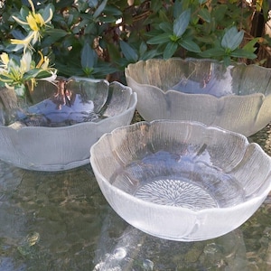 Könnte beinhalten: Drei klare Glasschalen mit einem texturierten, blütenblattartigen Außendesign und gewellten Rändern. Die Schalen weisen ein strahlenförmiges Muster auf dem inneren Boden auf, das ein florales Aussehen erzeugt. Das Glas hat eine mattierte Oberfläche.