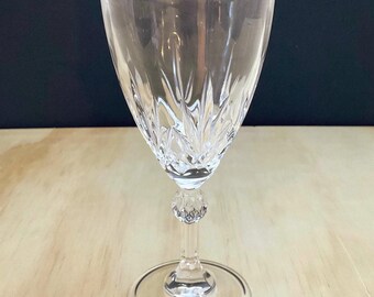 May include: A clear crystal wine glass featuring a vertical cut pattern on the bowl, a faceted spherical node on the stem, and a smooth circular base. The glass has a tapered silhouette and a polished finish, reflecting light through its facets.