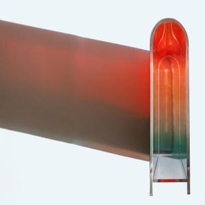 Peut inclure: Une sculpture abstraite moderne avec un dégradé de couleurs. Elle présente un élément vertical rectangulaire à sommet arrondi, passant du rouge au vert. Une longue forme angulaire projette une ombre.