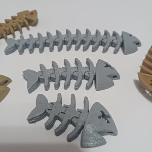 May include: Three gray plastic fish skeletons, each with a different size and shape. The skeletons are made of articulated pieces that can be moved.