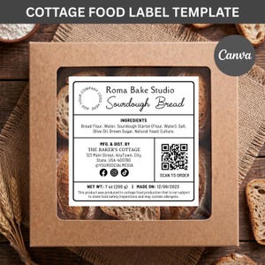 Op de afbeelding: Een vierkante bruine kartonnen doos met een doorzichtig venster met zuurdesembrood. Een wit rechthoekig etiket bevat de tekst Roma Bake Studio Sourdough Bread, een ingrediëntenlijst, fabrikantgegevens, een QR-code en een gewicht van 200 g.