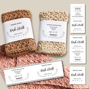 Pode incluir: Panos de prato de crochê em tons de marrom, bege e rosa, com etiquetas brancas. As etiquetas dizem "Dish Cloth" e incluem instruções de lavagem e opções de tamanho. Feito de 100% algodão.