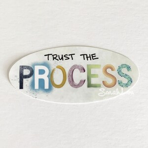 Może przedstawiać: Okrągła naklejka z białym tłem i kolorowymi literami tworzącymi napis "TRUST THE PROCESS". Litery są w różnych odcieniach niebieskiego, zielonego, żółtego, fioletowego i pomarańczowego. Naklejka ma kropkowany, akwarelowy efekt.