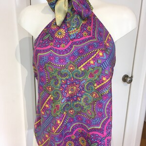 Puede incluir: Un top halter con un estampado geométrico colorido en tonos de rosa, morado, azul, verde y amarillo. El top tiene un lazo de satén dorado en el cuello.
