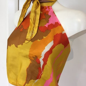 Puede incluir: Un top halter con un estampado abstracto colorido en tonos naranja, amarillo, rosa y marrón. El top tiene un lazo en el cuello y está hecho de una tela sedosa.