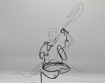 May include: Wire sculpture of a person kayaking on a piece of driftwood. The sculpture is made of black wire and is set against a white background.