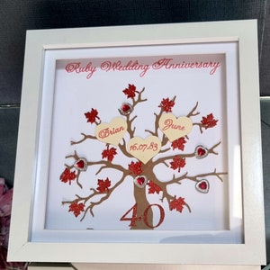 May include: A white framed picture with a red and gold glitter tree with red hearts and the words "Ruby Wedding Anniversary", "Brian", "June", "16.07.83", and "40" on it.