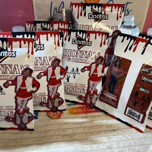 May include: Several white Doritos chip bags with red and black dripping paint designs. The bags are personalized with a child's image and the text "Rionna's 11th Birthday". Additional tags are also visible.
