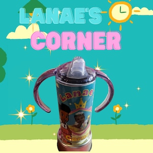 May include: A children's sippy cup with a teal background and the text "Lanae's Corner" in blue and pink. The cup features a cartoon illustration of a child and a crown. The cup has pink handles and a clear lid.