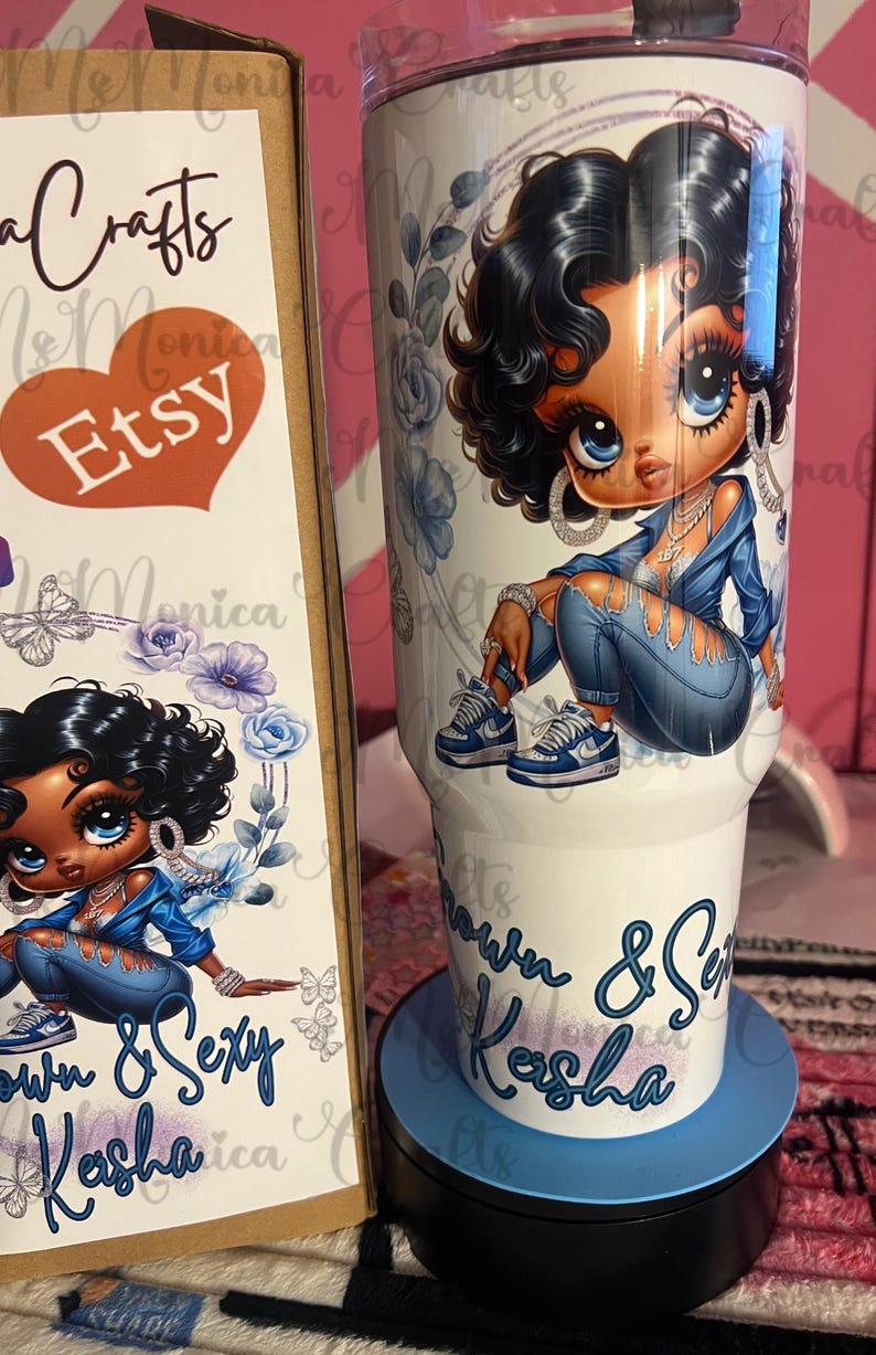 May include: A white tumbler with a cartoon illustration of a woman in a denim outfit, with blue floral accents. The tumbler has the text "Own & Sexy Kasha" in blue script. A matching box with the Etsy logo is also visible.