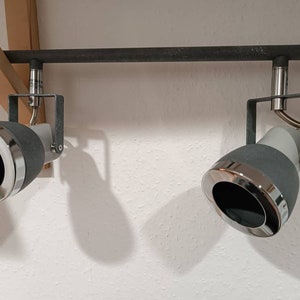 Könnte beinhalten: Zwei schwarze und silberne Schienenstrahler mit verstellbaren Köpfen sind an einer schwarzen Schiene montiert.