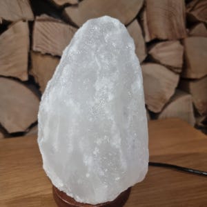 May include: A white Himalayan salt lamp with a wooden base. The lamp is shaped like a tall, thin rock.