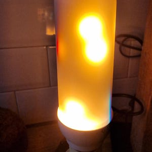 May include: A white light bulb with a flickering flame effect. The bulb is lit and casting a warm yellow glow.