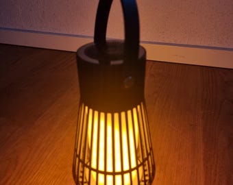 May include: A black metal lantern with a handle and a caged light source. The light is on and emits a warm yellow glow.