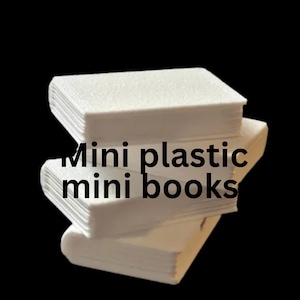 May include: A stack of three white rectangular plastic mini books with visible page edges and a smooth finish. The text "Mini plastic mini books" is printed in black across the center of the stack, clearly visible against the white surface.