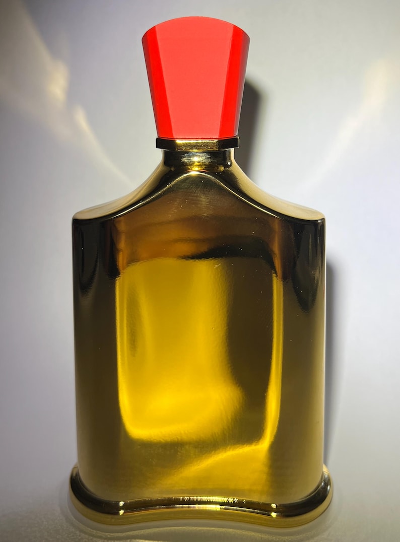 May include: A gold-colored perfume bottle with a red cap. The bottle has a rectangular shape with rounded edges and a shiny, reflective surface. The cap is a trapezoid shape.