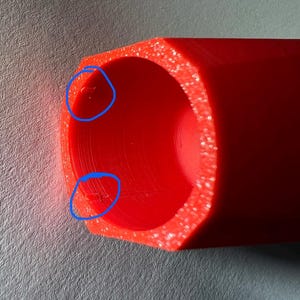 May include: Close-up of a bright red, cylindrical object with a hexagonal outer shape. The interior is hollow, and the edges have a slightly textured appearance. The object is made of a solid, opaque material.