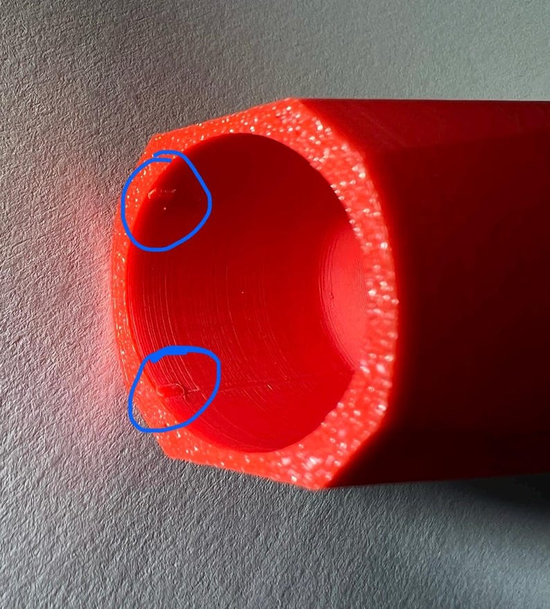 May include: Close-up of a bright red, cylindrical object with a hexagonal outer shape. The interior is hollow, and the edges have a slightly textured appearance. The object is made of a solid, opaque material.
