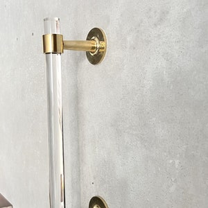 May include: A gold door handle with a clear acrylic bar. The handle is mounted on a wall.