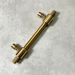 Könnte beinhalten: Ein goldfarbener, metallischer Schrankgriff mit zylindrischem Design und abgerundeten Enden. Der Griff hat eine glatte, polierte Oberfläche.