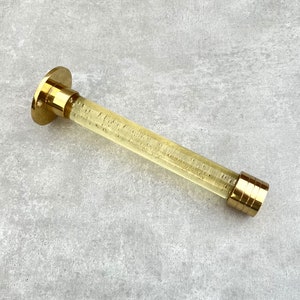 May include: A gold-toned metal curtain rod with a clear, textured glass tube. The tube has a gold-toned metal end cap.