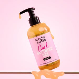 Könnte beinhalten: Eine Flasche TMA Curl Defining Gel, 240 ml, mit einem schwarzen Pumpspender und einem rosa Etikett. Das Etikett zeigt den Markennamen und Produktdetails in Weiß und Rosa. Das Gel hat eine goldene Farbe, etwas tropft aus der Flasche.