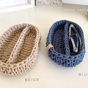 May include: Two oval-shaped, woven storage baskets. One is beige with a brown leather accent, the other is blue, holding eyeglasses. The baskets are divided into two compartments. The word "BEIGE" is written below the beige basket, and "BLUE" is written below the blue basket.