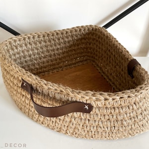 Peut inclure: Un panier en jute naturel avec une poignée en cuir marron. Le panier est tissé en forme de losange et a une base en bois.