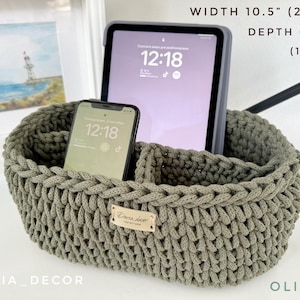 Peut inclure: Panier de rangement en crochet de couleur olive avec deux compartiments pour organiser les objets. Le panier mesure 27 cm de large et 17 cm de profondeur. Il est présenté avec un téléphone et une tablette à l'intérieur.