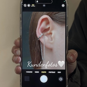 K&ouml;nnte beinhalten: Nahaufnahme eines Ohrs mit einem silbernen Ohrclip und einer daran h&auml;ngenden Kette. Das Bild wurde auf einem Smartphone-Bildschirm aufgenommen, auf dem das Wort "Kundenfotos" und ein wei&szlig;es Herz-Emoji zu sehen sind.