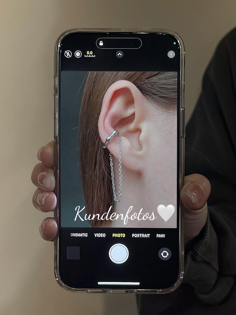 K&ouml;nnte beinhalten: Nahaufnahme eines Ohrs mit einem silbernen Ohrclip und einer daran h&auml;ngenden Kette. Das Bild wurde auf einem Smartphone-Bildschirm aufgenommen, auf dem das Wort "Kundenfotos" und ein wei&szlig;es Herz-Emoji zu sehen sind.