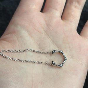 K&ouml;nnte beinhalten: Eine silberne Kettenkette mit einem einzigartigen, abstrakten, offenen Kreisanh&auml;nger.