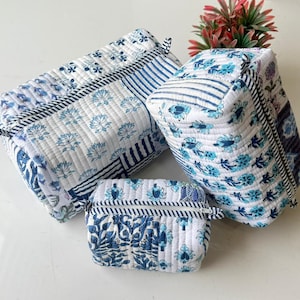 May include: Three quilted cosmetic bags in different sizes, with a white base and blue floral and striped designs. The bags are rectangular with zip closures and small fabric loops, ideal for toiletries.