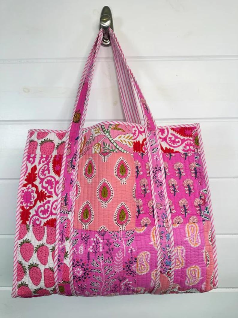 May include: A pink and white patchwork tote bag with a quilted design. The bag has a large main compartment and two shorter handles.