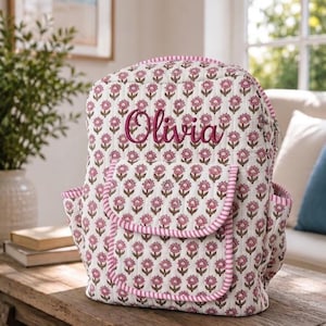 May include: A quilted backpack featuring a repeating pink and green floral pattern on a white background. The front pocket has a pink and white striped trim, and the name Olivia is embroidered in dark pink script across the upper section.