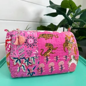 May include: Pink quilted makeup bag with a patchwork design featuring tigers, flowers, and geometric patterns. The bag has a tassel pull.