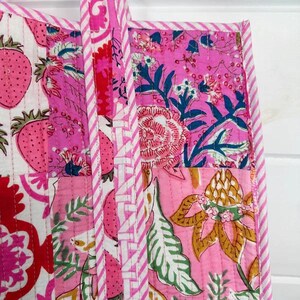 May include: A pink and white patchwork tote bag with floral and strawberry patterns. The bag has a white and pink striped handle.