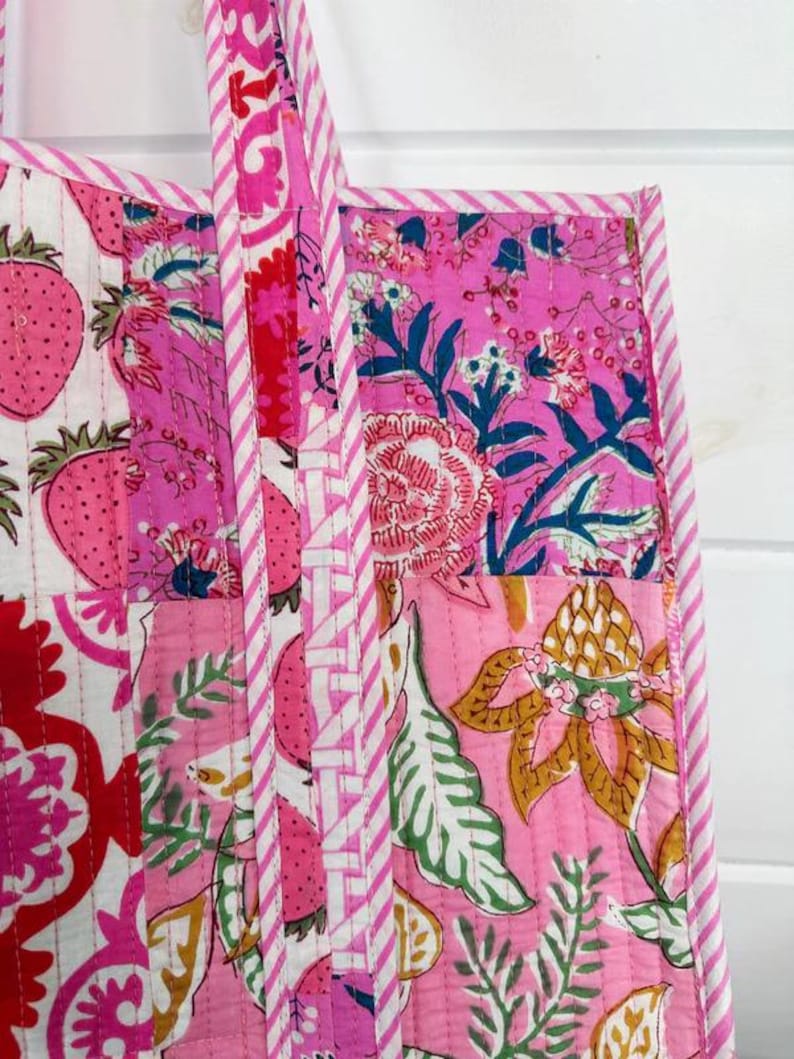 May include: A pink and white patchwork tote bag with floral and strawberry patterns. The bag has a white and pink striped handle.