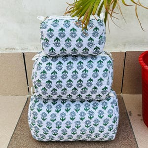 Puede incluir: Tres bolsas de cremallera de tela blanca con un estampado floral verde y azul. Las bolsas están apiladas una encima de la otra.