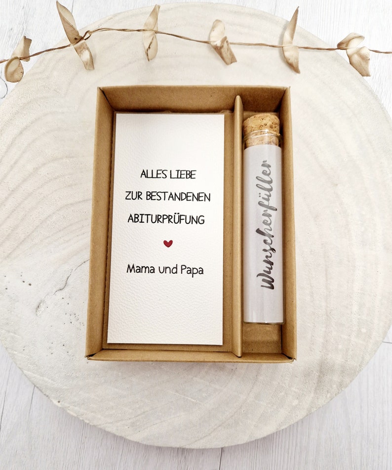 May include: A small brown box with a white card inside that reads "Alles Liebe zur bestandenen Abiturpr&uuml;fung" with a red heart and "Mama und Papa".  The box also contains a glass vial with a cork stopper and a white label that reads "Wunschersch&ouml;pfer".