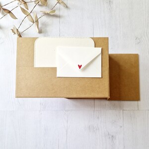 May include: A brown cardboard box with a white envelope inside. The envelope has a small red heart on the front.