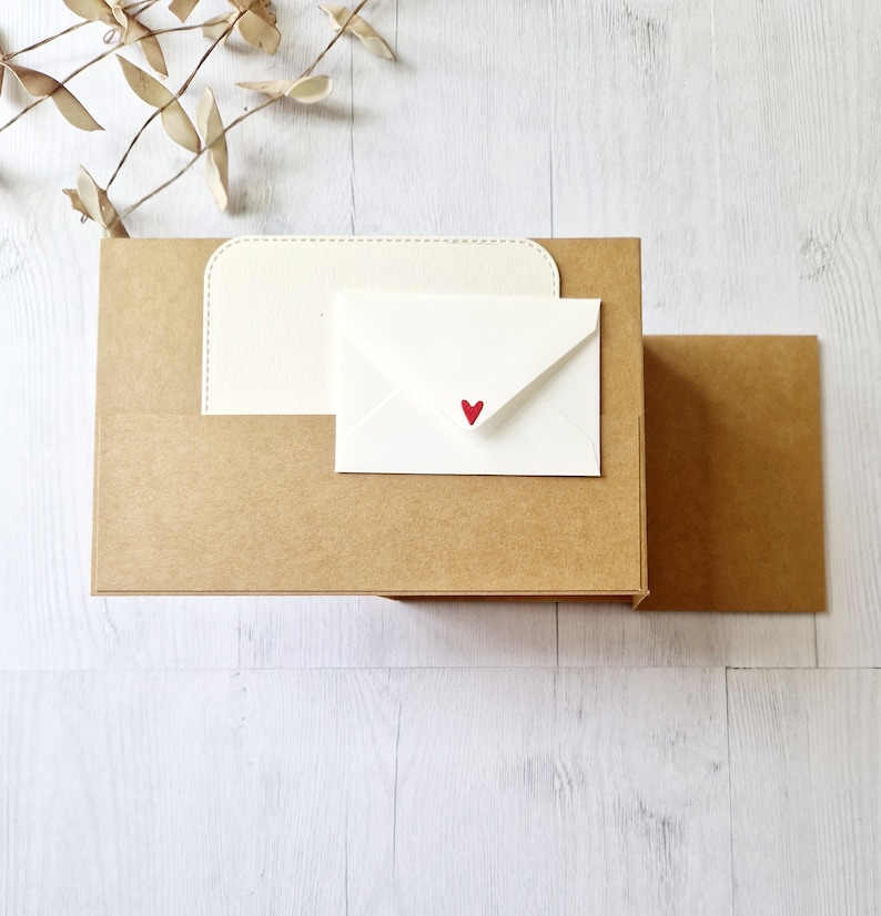 May include: A brown cardboard box with a white envelope inside. The envelope has a small red heart on the front.
